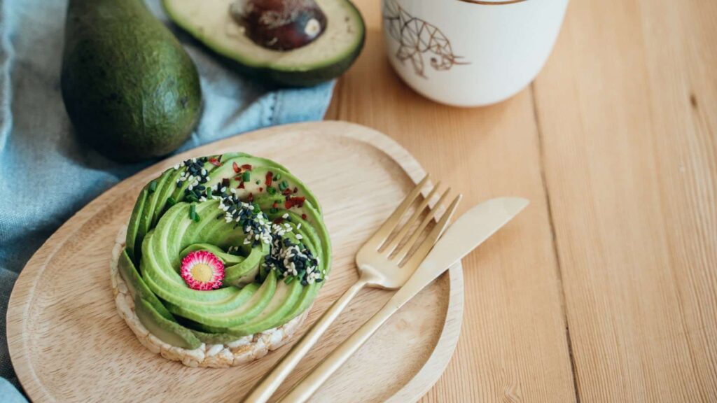 Avocado spread out into a flower shape on a wooden plate with a gold fork and butter knife