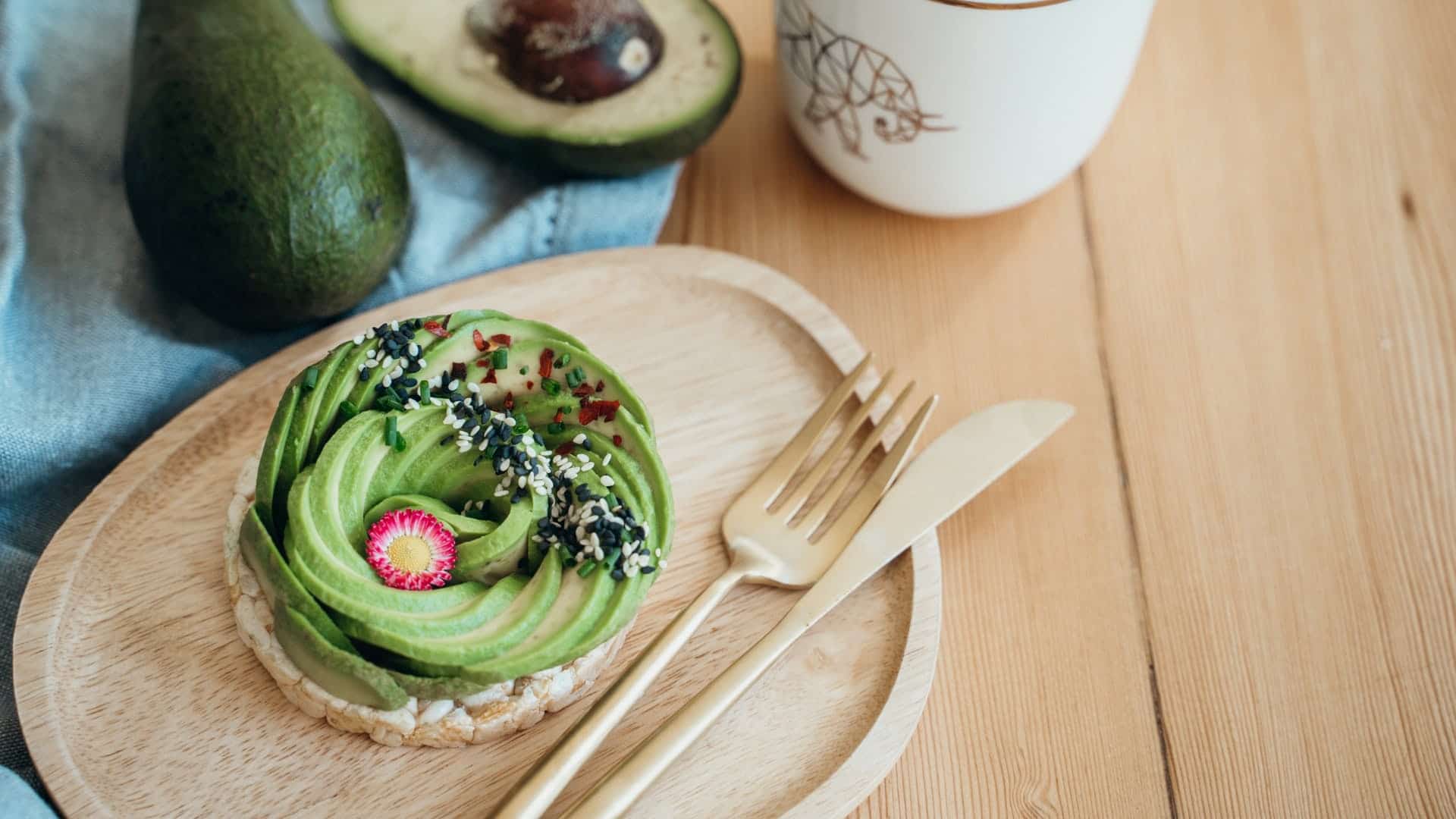 Avocado spread out into a flower shape on a wooden plate with a gold fork and butter knife