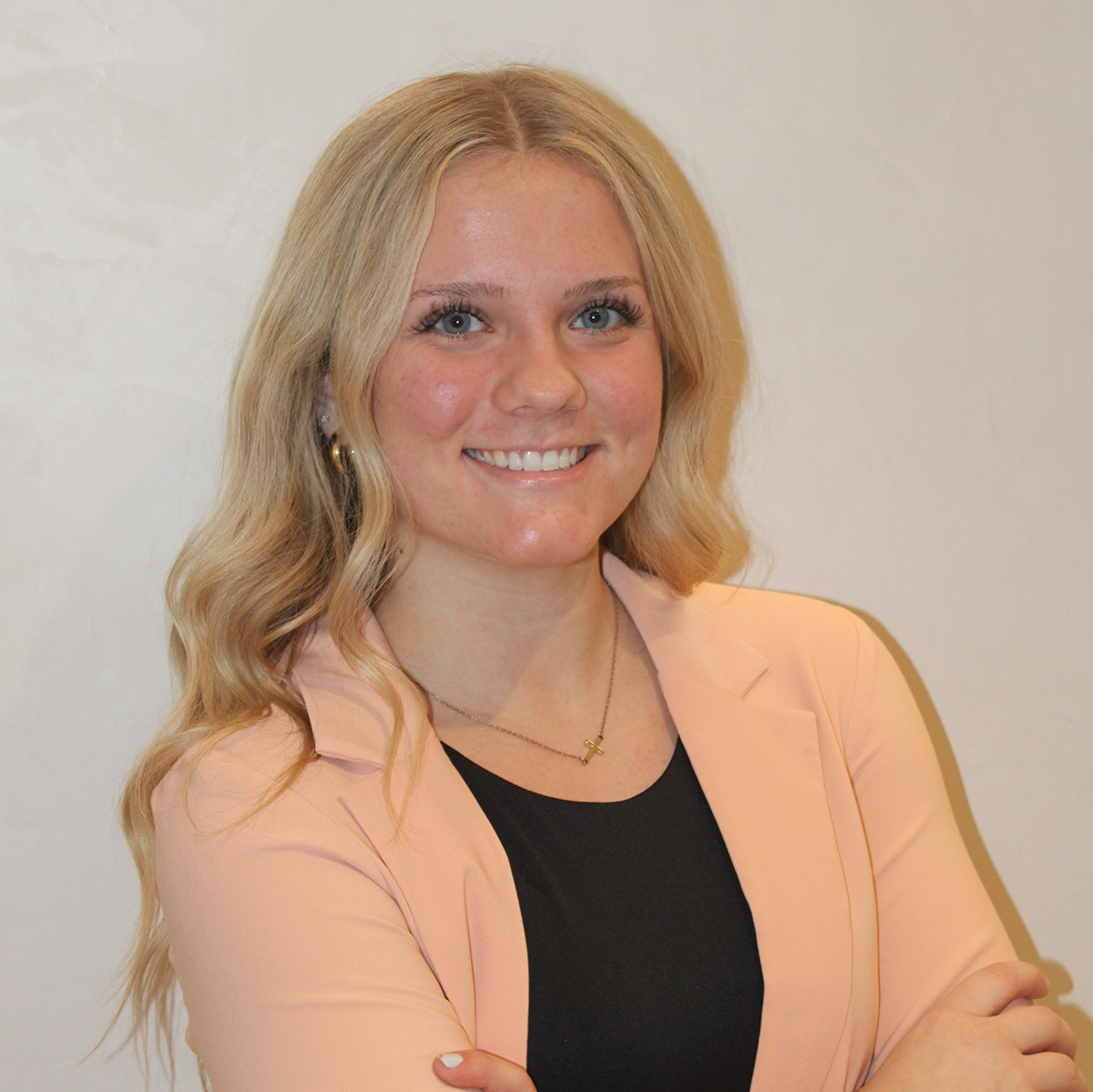 A young lady smiling at the camera in a peach blazer.